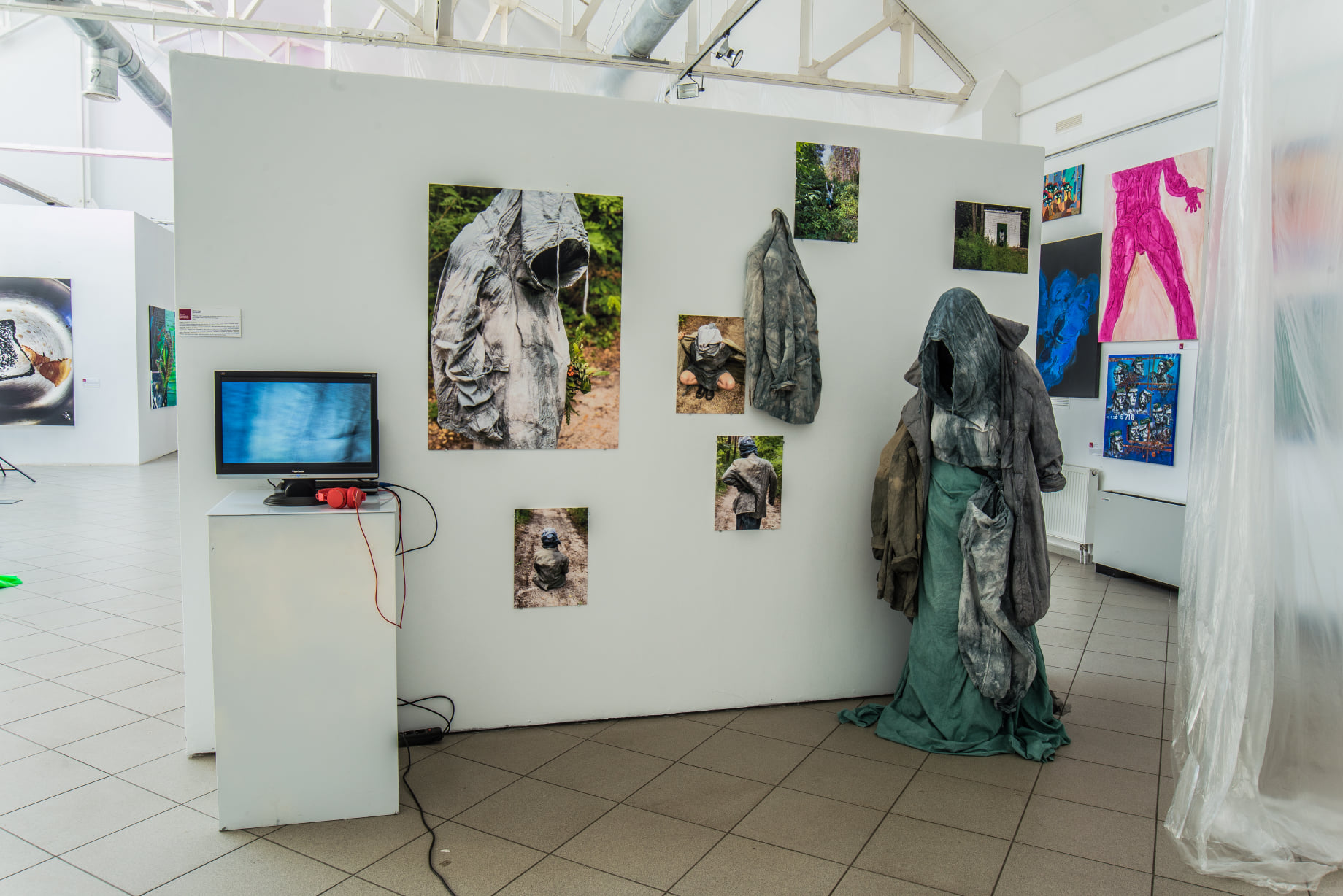 Le Facteur ISRS — exhibition view with stone-textured garments, photographs and a video monitor